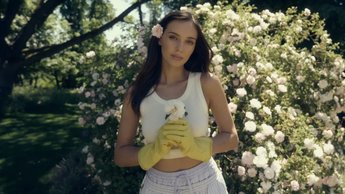 Charlotte Ella Gottová stojí před keřem s květinami.