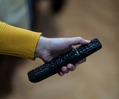Close-up of a hand with a yellow-sleeved sweater gripping a black TV remote, showing colorful buttons