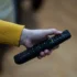 Close-up of a hand with a yellow-sleeved sweater gripping a black TV remote, showing colorful buttons
