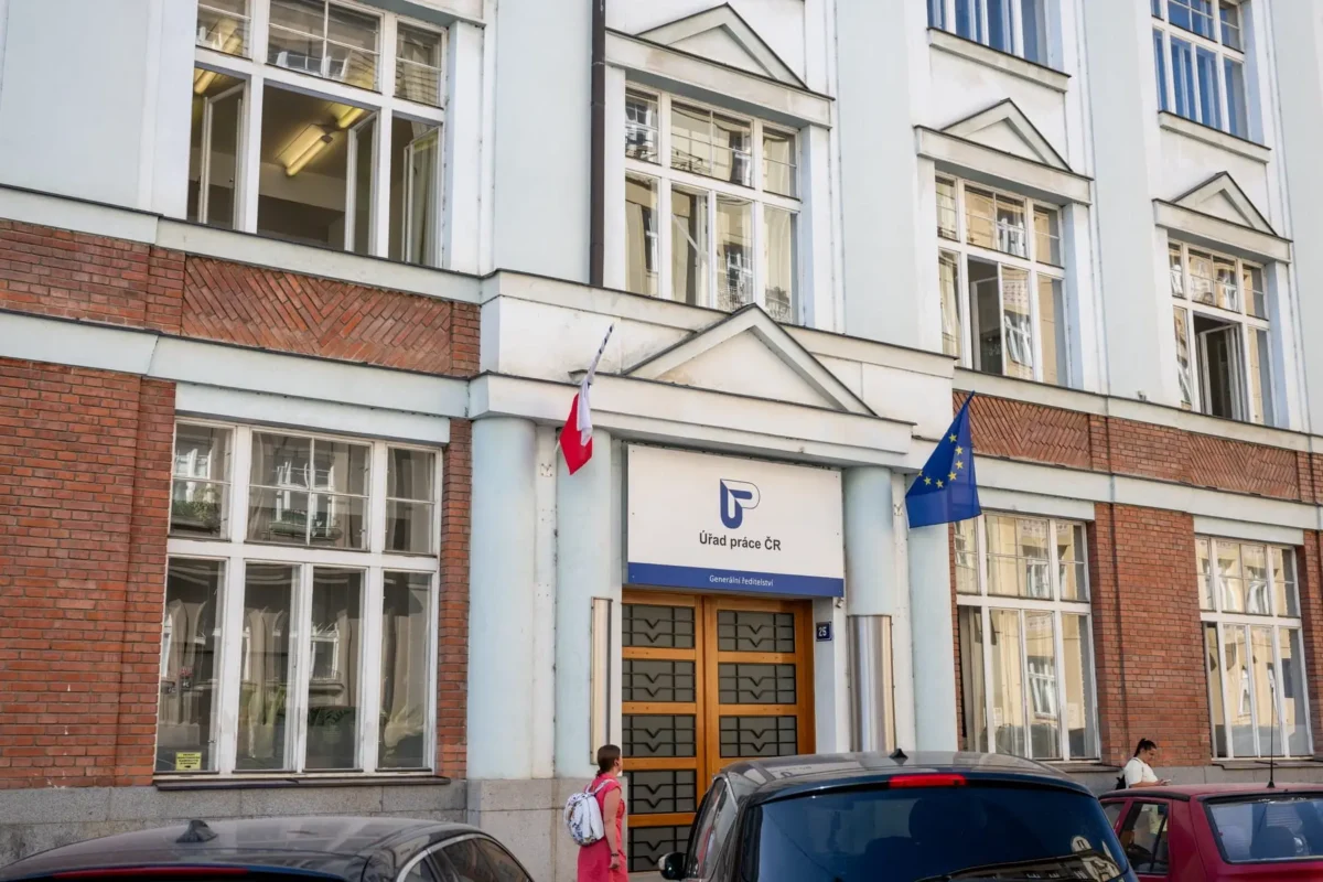 Front of a government office building with Czech and EU flags; sign reads Úřad práce ČR.