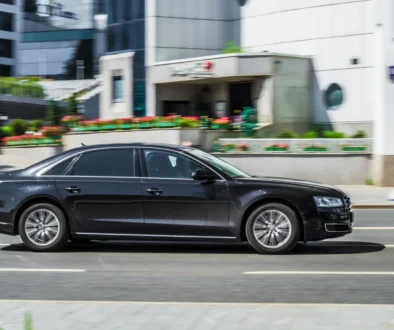 Black luxury sedan driving past urban buildings in motion blur, street scene with colorful planters and pedestrians in the background