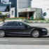 Black luxury sedan driving past urban buildings in motion blur, street scene with colorful planters and pedestrians in the background