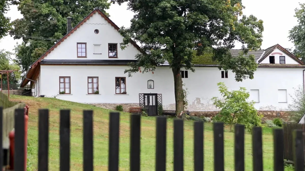 Statek s bílou fasádou, trávníkem, stromy a plotem během dne