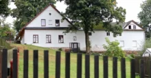 Statek s bílou fasádou, trávníkem, stromy a plotem během dne