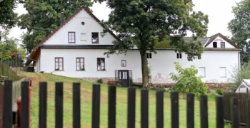 Statek s bílou fasádou, trávníkem, stromy a plotem během dne