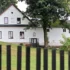 Statek s bílou fasádou, trávníkem, stromy a plotem během dne