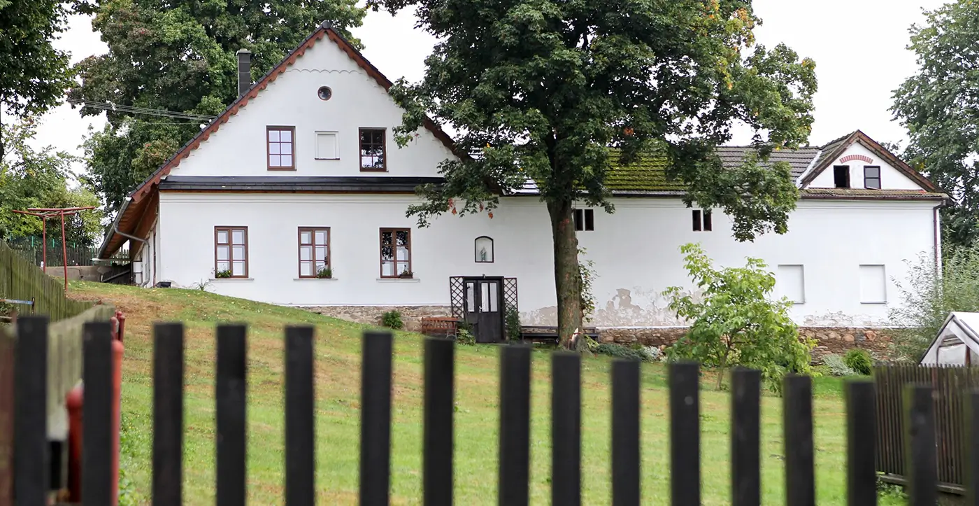 Statek s bílou fasádou, trávníkem, stromy a plotem během dne