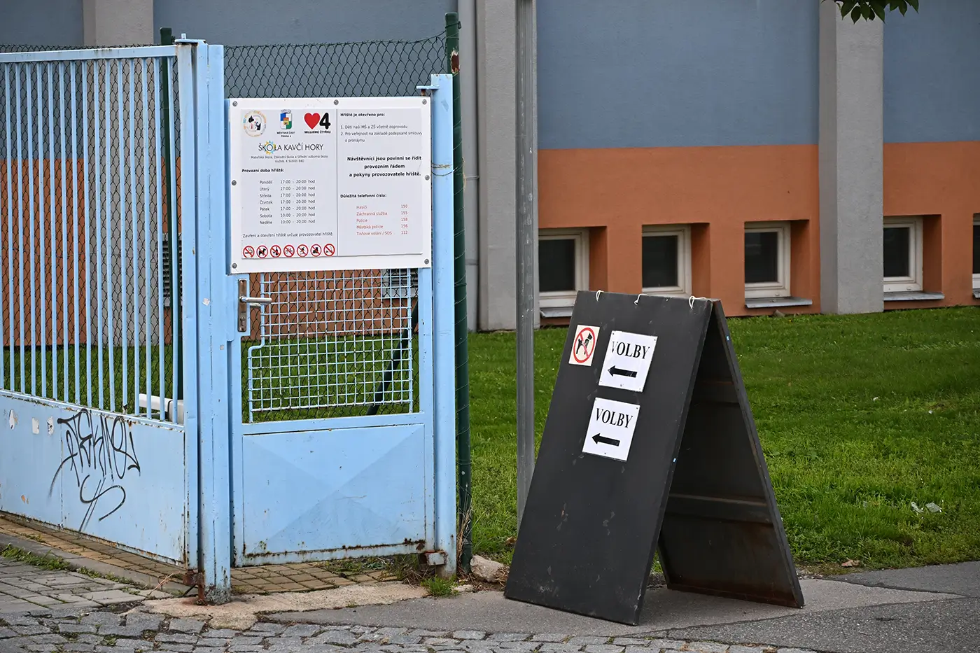 shutterstock_2685615629 | TVGURU.cz Cedule se směrovkami k volbám stojí před světle modrou brankou