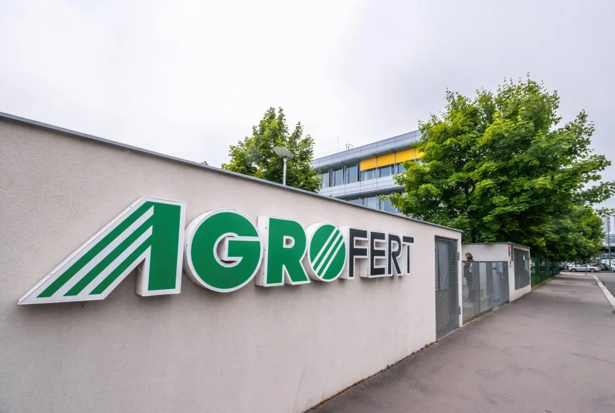 Exterior wall with a large AGROFERT sign in green letters and a striped logo, set beside a sidewalk and trees in the background.