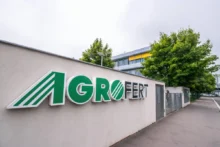 Exterior wall with a large AGROFERT sign in green letters and a striped logo, set beside a sidewalk and trees in the background.