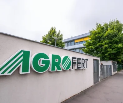 Exterior wall with a large AGROFERT sign in green letters and a striped logo, set beside a sidewalk and trees in the background.
