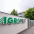 Exterior wall with a large AGROFERT sign in green letters and a striped logo, set beside a sidewalk and trees in the background.