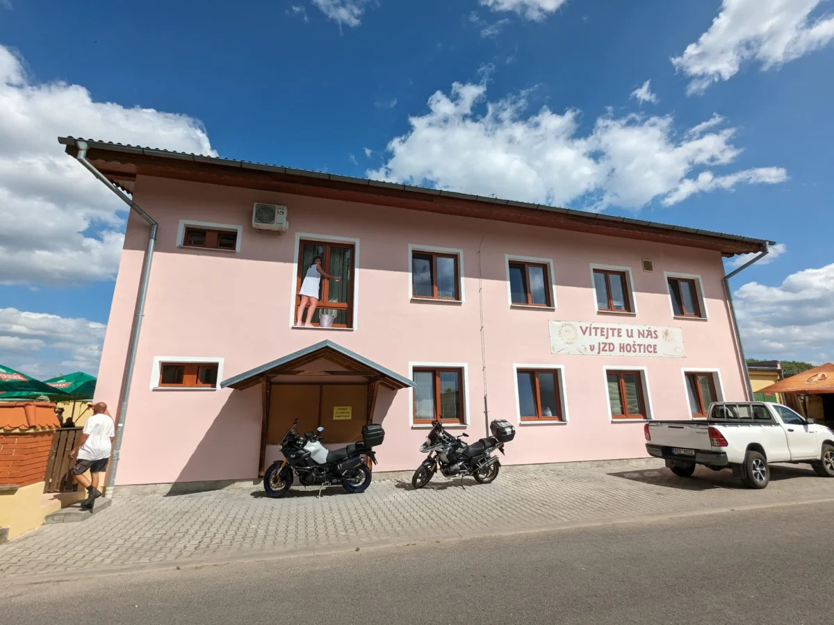 shutterstock_2340318389 1 | TVGURU.cz Pink two-story building with a sign in a foreign language, parked motorcycles in front, blue sky and clouds above.