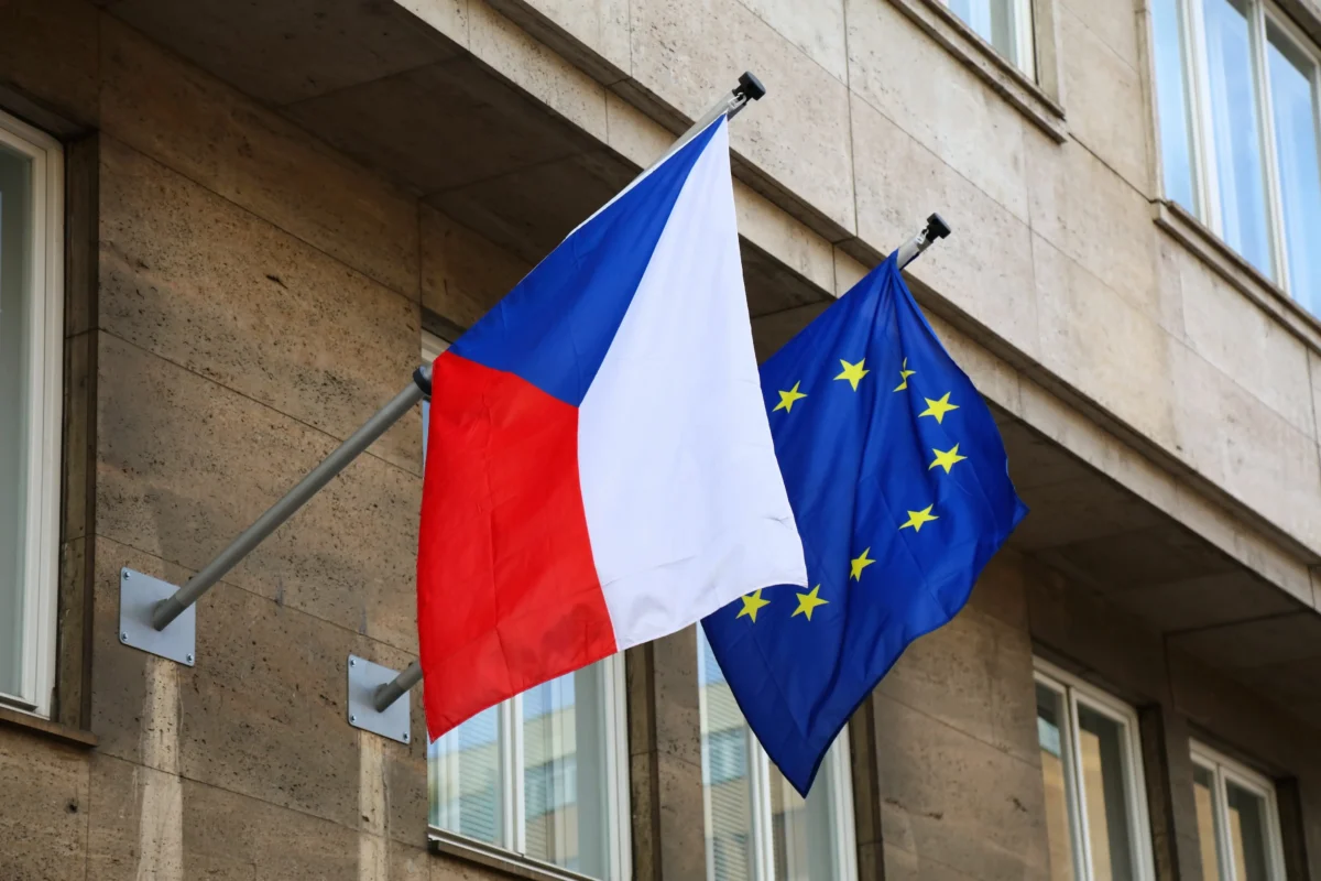 shutterstock_2491336267 1 | TVGURU.cz Flagpole with the Czech Republic flag and the European Union flag fluttering outside a beige stone building of windows.