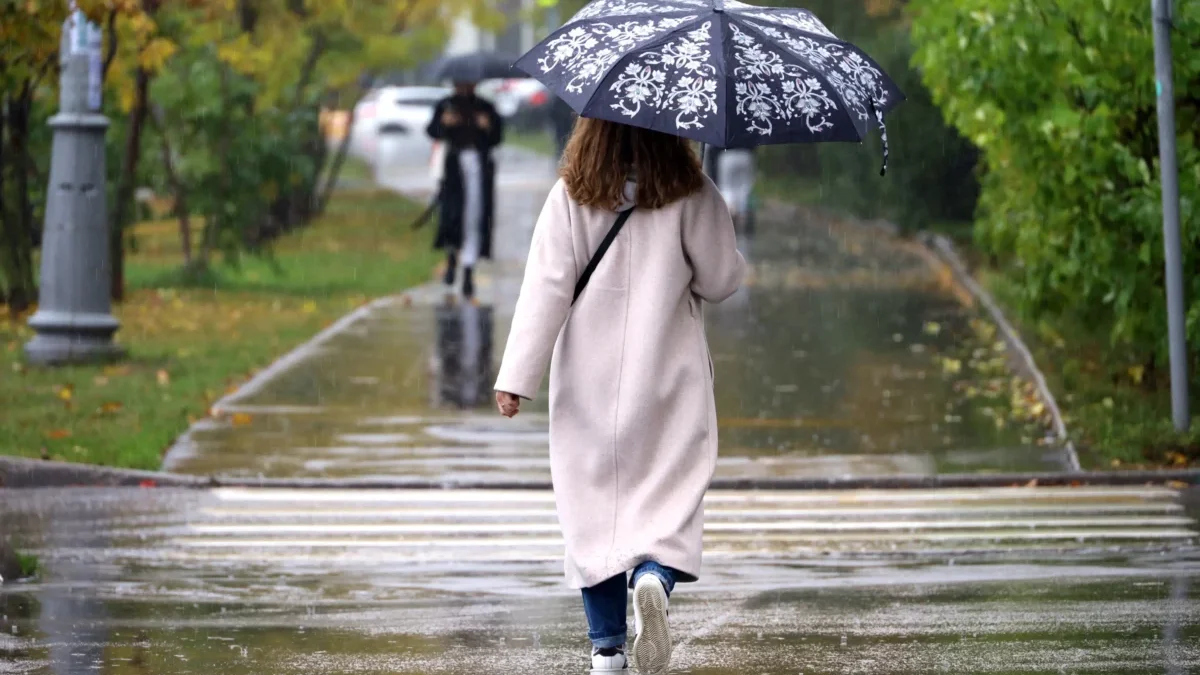 Žena jde po silnici s deštníkem.