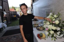 Mladý muž v černém tričku upravuje květinovou vazbu.