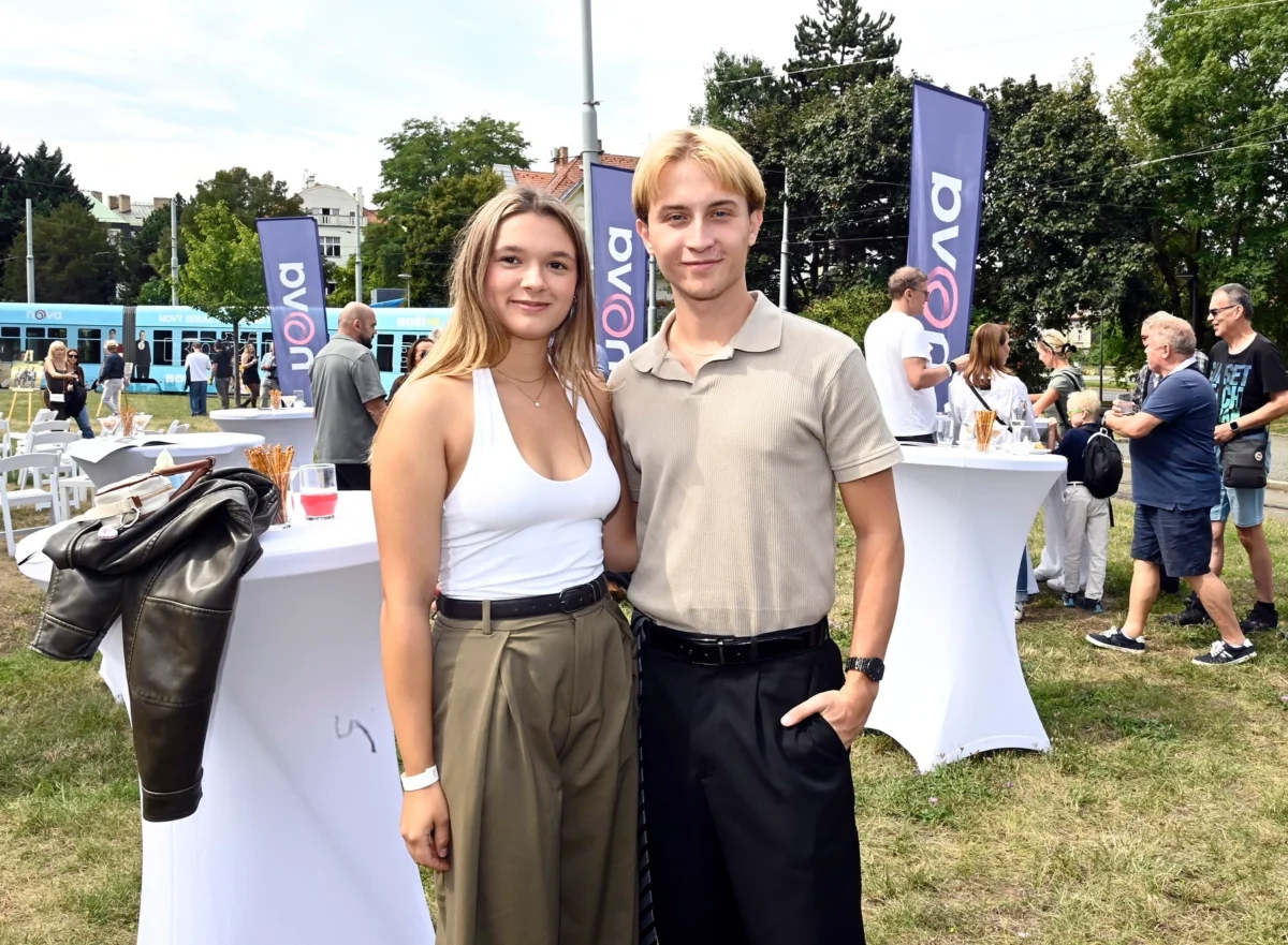 Dva mladí lidé v letním oblečení na louce s bílými bistro stolky a logy televize Nova