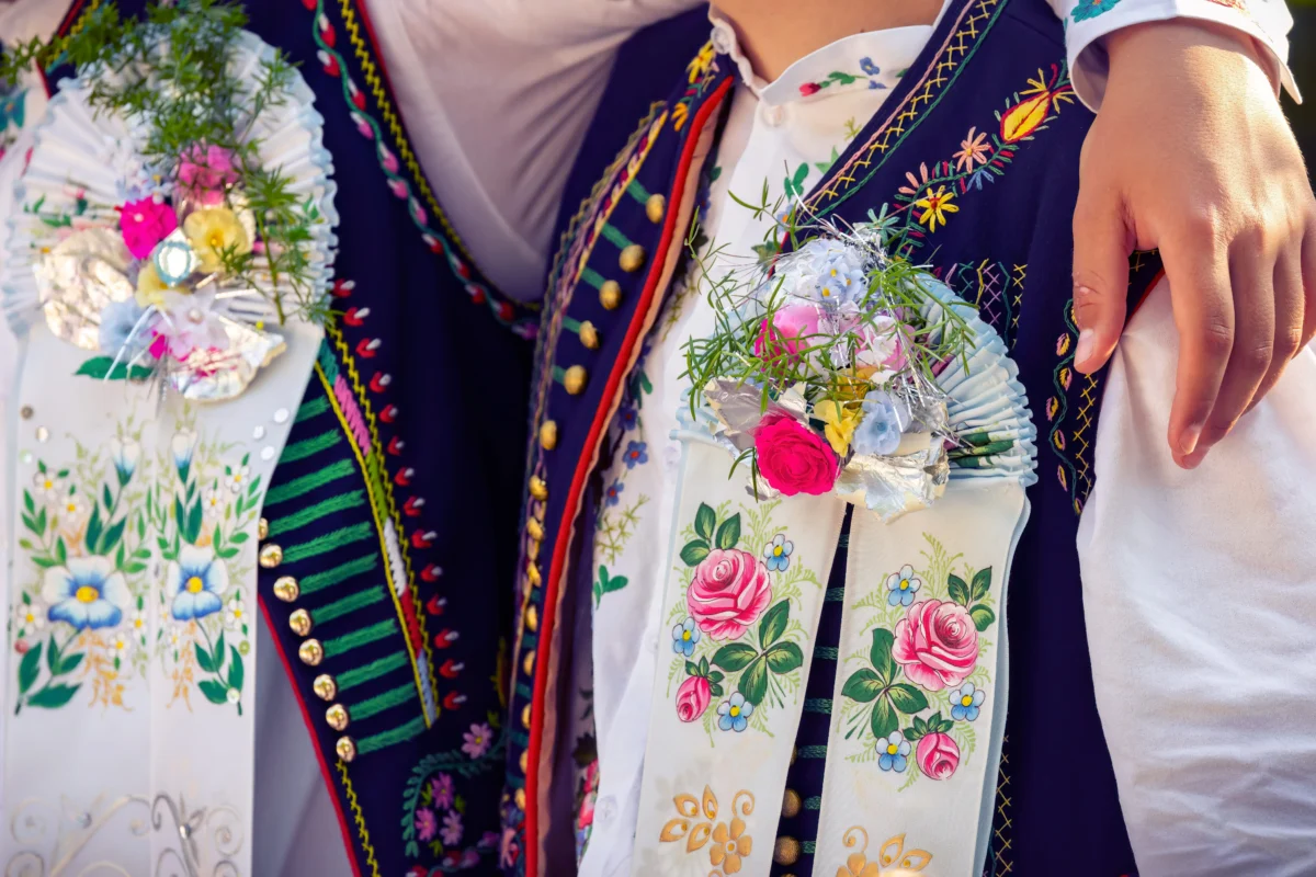 Close-up of people wearing traditional embroidered folk costumes with floral sashes and ribbons.