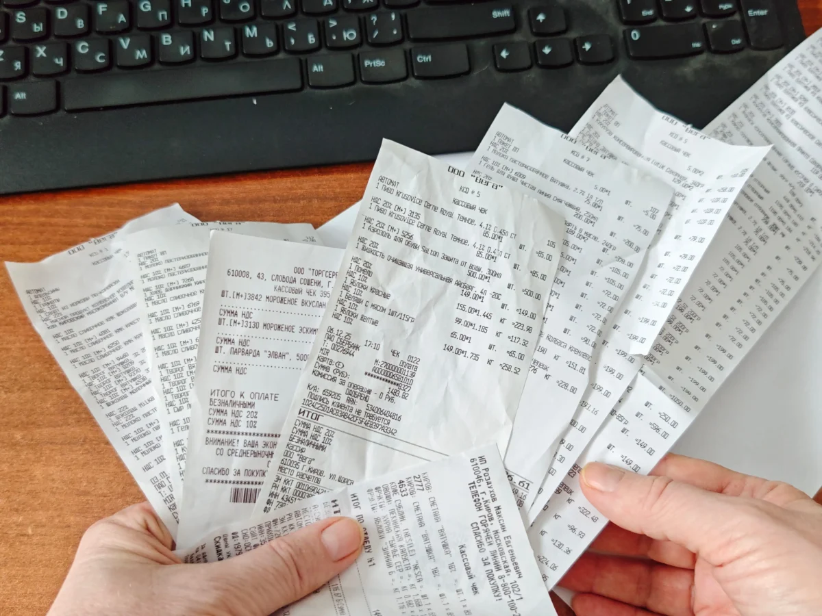shutterstock_2734892833 1 | TVGURU.cz Hands holding several crumpled receipts filled with Russian text on a wooden desk, a black keyboard visible in the background.