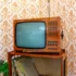 Vintage wooden TV with a curved screen on a shelf, against orange floral wallpaper and a stack of records nearby.