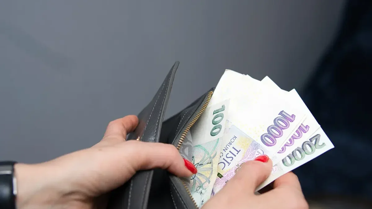 Žena s červeně nalakovanými nehty drží v ruce peněženku a vytahuje z ní papírové bankovky