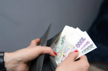 Žena s červeně nalakovanými nehty drží v ruce peněženku a vytahuje z ní papírové bankovky