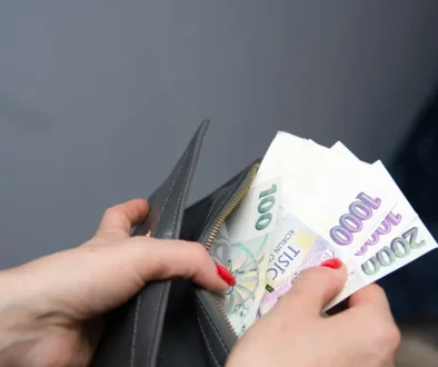 Žena s červeně nalakovanými nehty drží v ruce peněženku a vytahuje z ní papírové bankovky