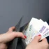 Žena s červeně nalakovanými nehty drží v ruce peněženku a vytahuje z ní papírové bankovky