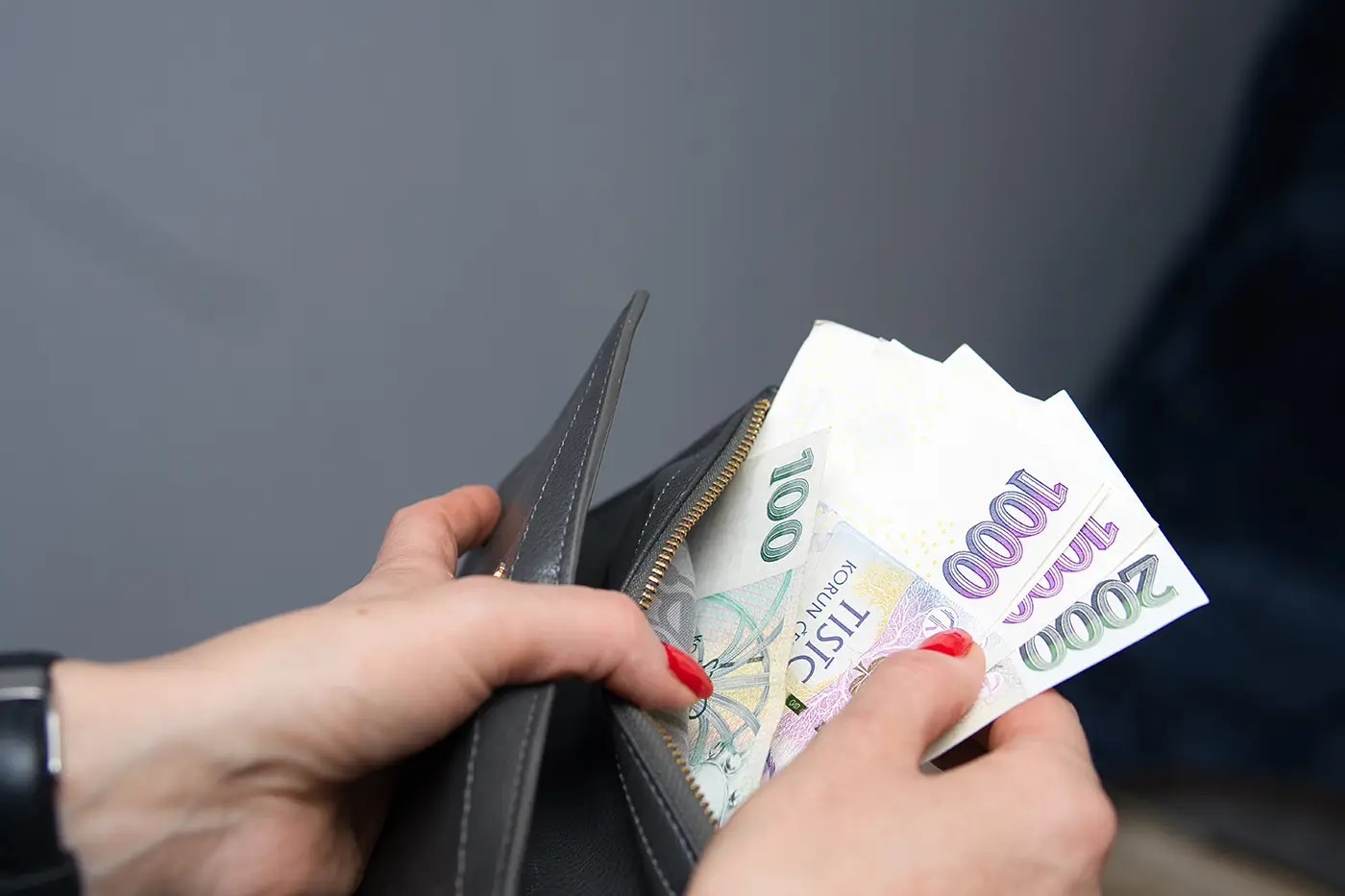 Žena s červeně nalakovanými nehty drží v ruce peněženku a vytahuje z ní papírové bankovky