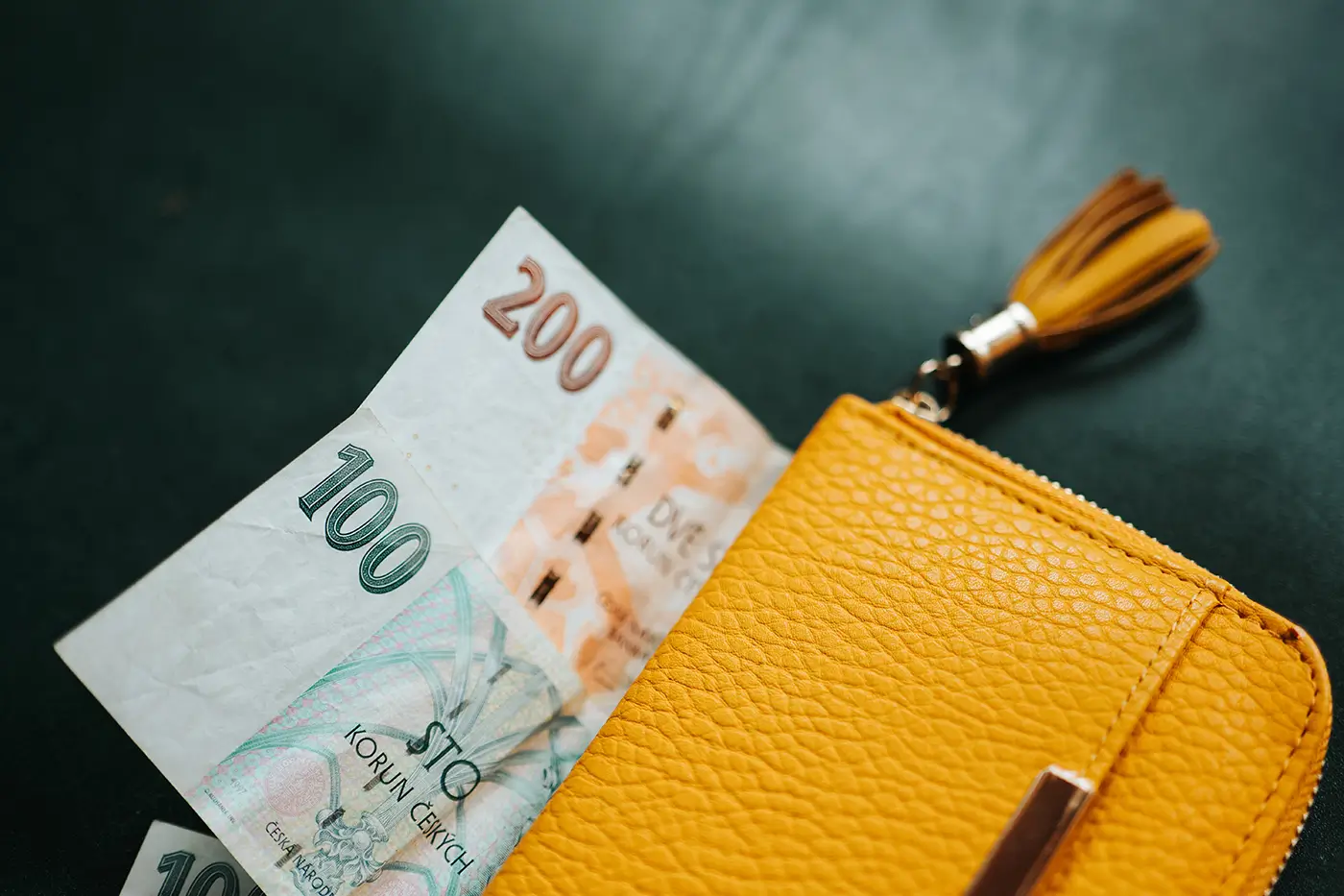 shutterstock_2729410333 | TVGURU.cz Na stole leží žlutá peněženka a z ní vykukují dvě české bankovky