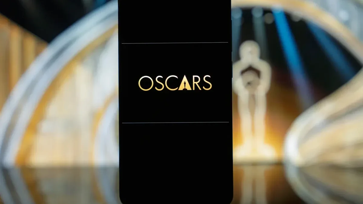Na skleněném stole stojí mobilní telefon s názvem prestižní filmové ceny a za ním je filmová soška