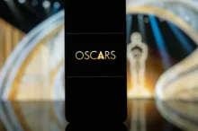 Na skleněném stole stojí mobilní telefon s názvem prestižní filmové ceny a za ním je filmová soška