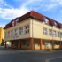Beige multi‑story building with red tiled roof and large windows on a cobblestone street under a blue sky.