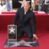 Vin Diesel kneels on a red carpet, holding his Hollywood Walk of Fame plaque in front of his star on the sidewalk.