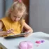 Malá holčička ve žlutém tričku sedí za stolem a dívá se do tabletu.