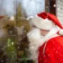 Muž v santa clausovském oblečení kouká v zimě do okna.