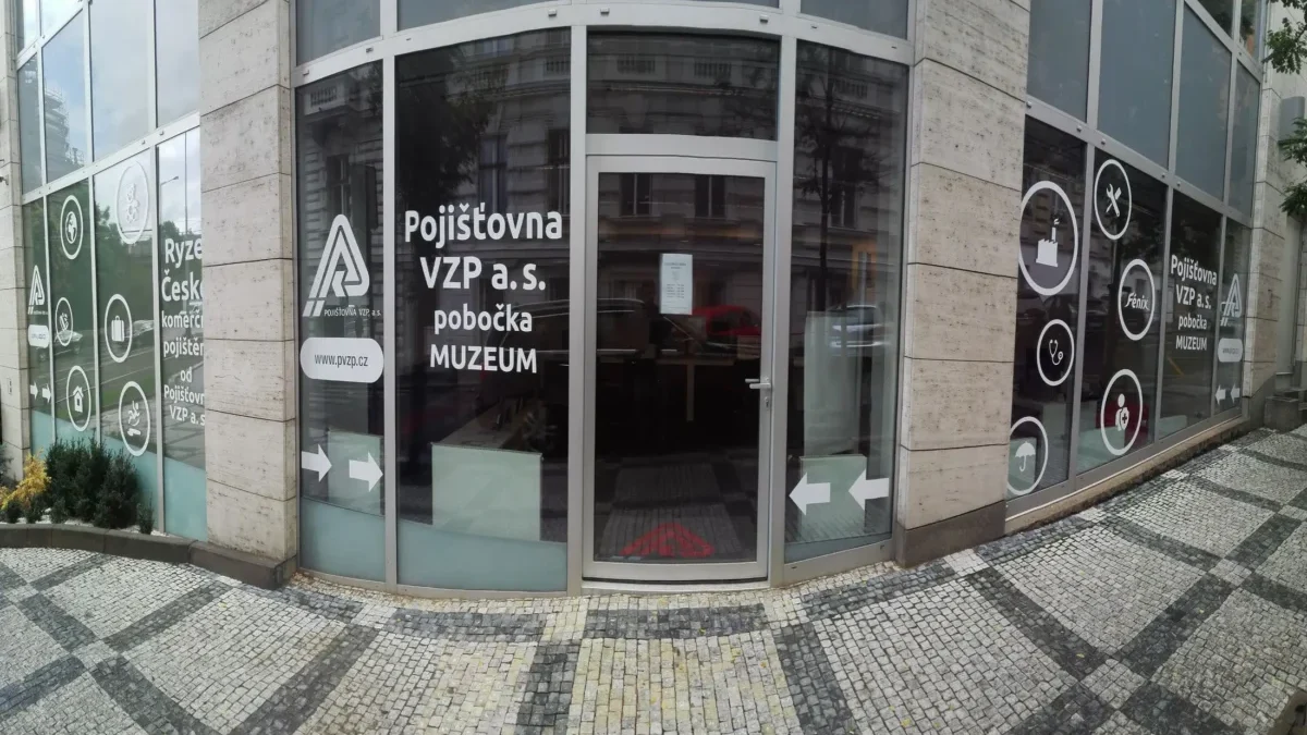 Front of Pojišťovna VZP a.s. branch with curved glass doors and MUZEUM signage on the windows