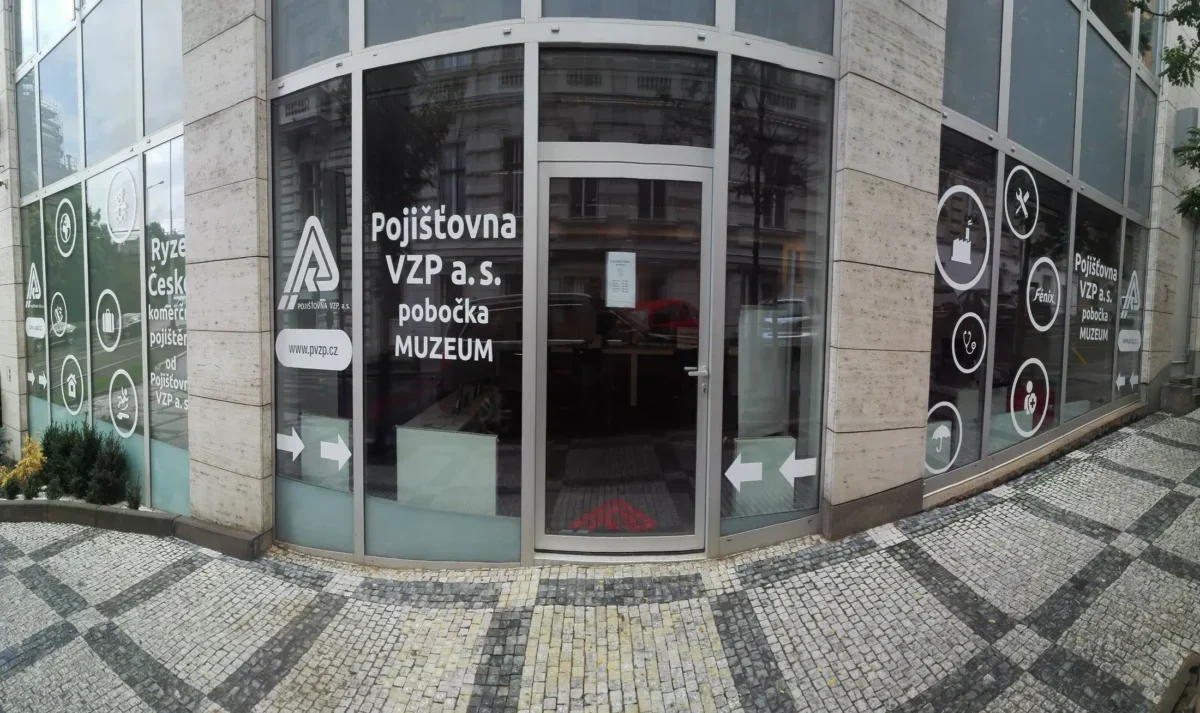 Front of Pojišťovna VZP a.s. branch with curved glass doors and MUZEUM signage on the windows