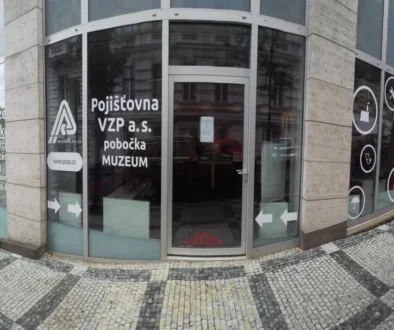 Front of Pojišťovna VZP a.s. branch with curved glass doors and MUZEUM signage on the windows