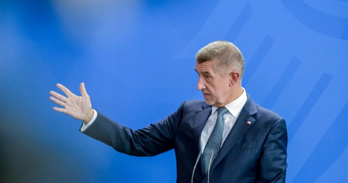 Gestikulující muž v tmavém obleku na modrém pozadí. Muž se mračí.