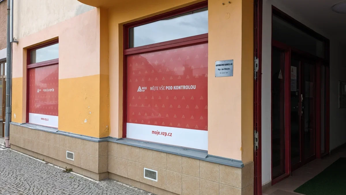 Budova domu s oranžovou fasádou, v přízemí jsou velké výkladní skříně, v nich nápis VZP