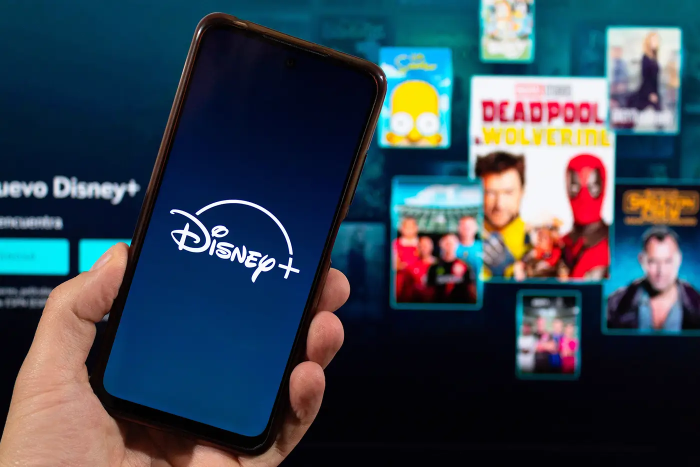 shutterstock_2594799287-2 | TVGURU.cz Člověk drží v ruce mobilní telefon s logem Disney+ a za tím se na televizi promítá spuštěná streamovací platforma