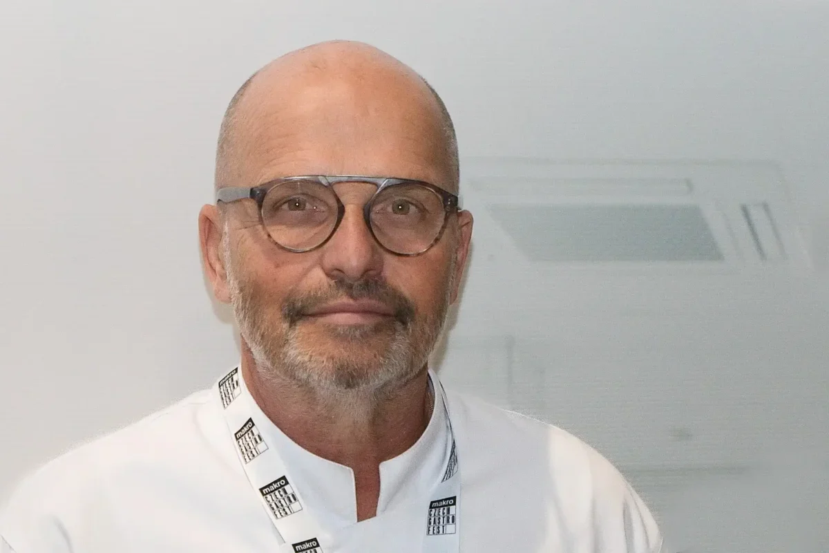Portrait of a bald man with round glasses and light stubble, wearing a white coat and a Makro lanyard against a plain background.