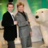 Two men in suits posing and fist-bumping beside a large white polar bear statue indoors with a green backdrop.