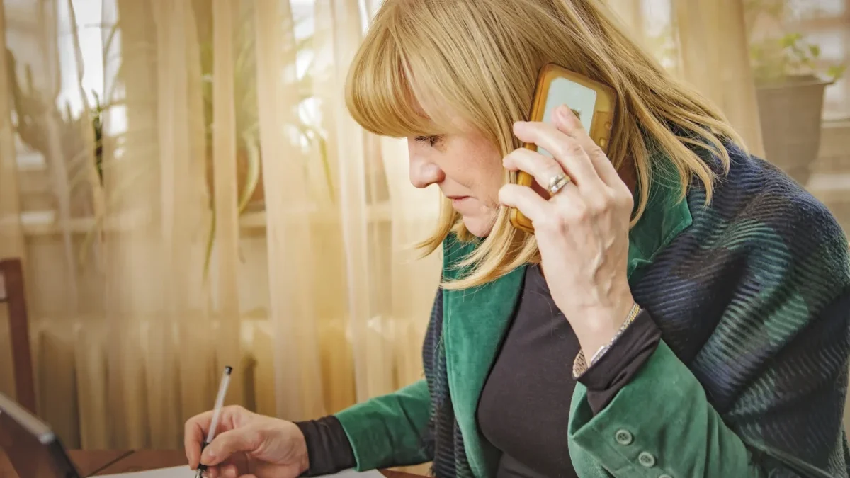 Žena telefonuje a sedí u stolu.