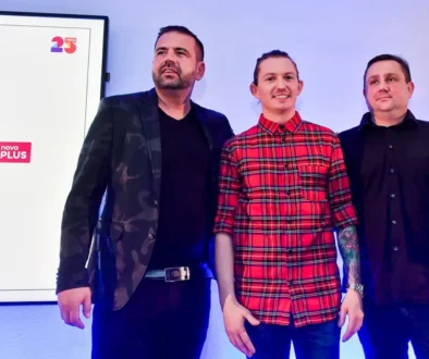 Tři muži stojí na podiu a za nimi na stěně visí promítací obrazovka