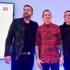 Tři muži stojí na podiu a za nimi na stěně visí promítací obrazovka