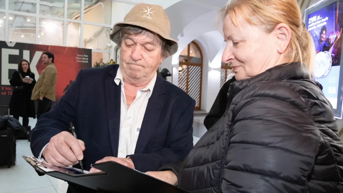 Muž v hučce podepisuje památník starší ženě