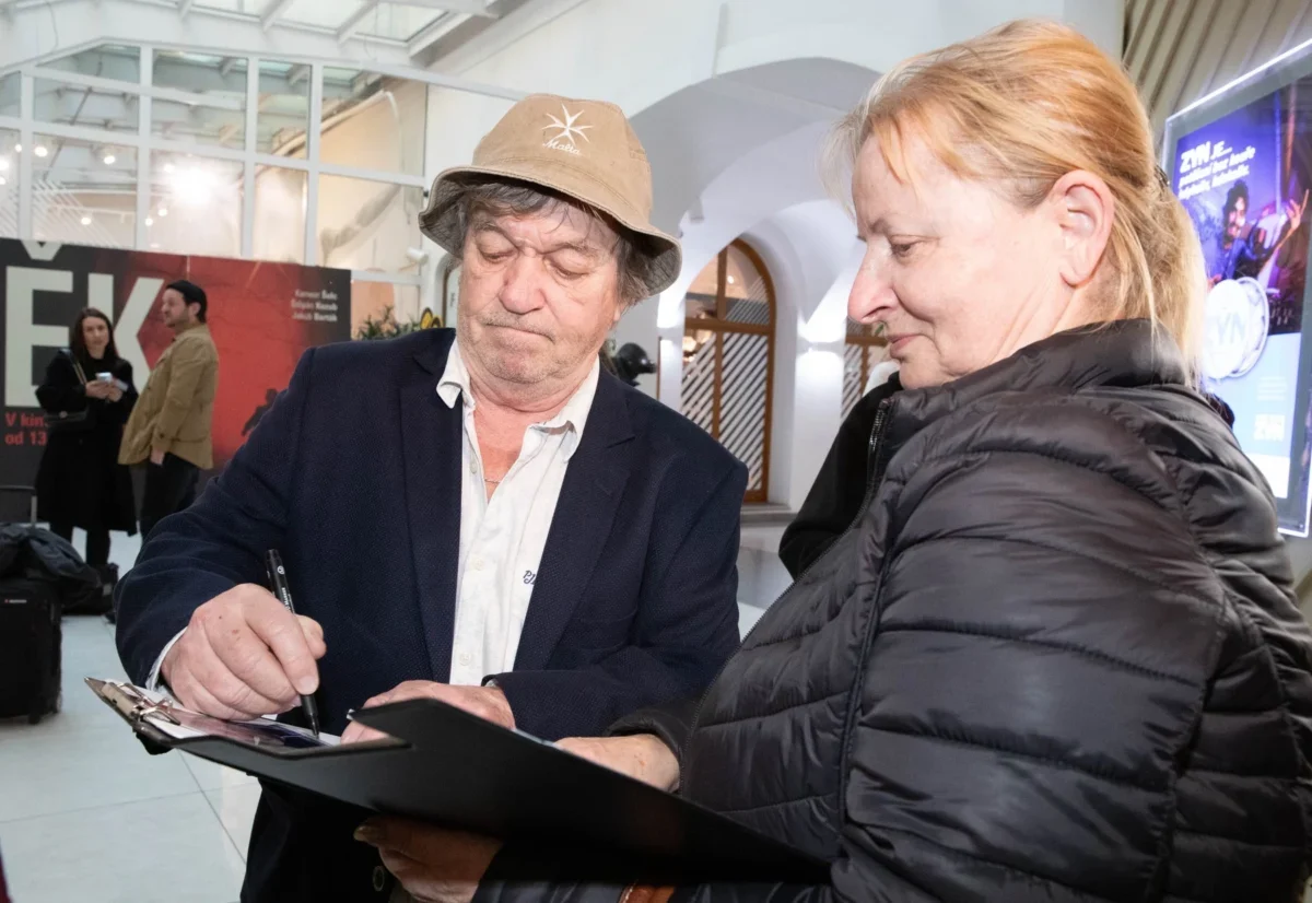 Muž v hučce podepisuje památník starší ženě