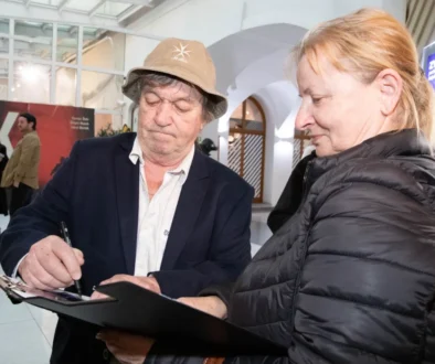 Muž v hučce podepisuje památník starší ženě